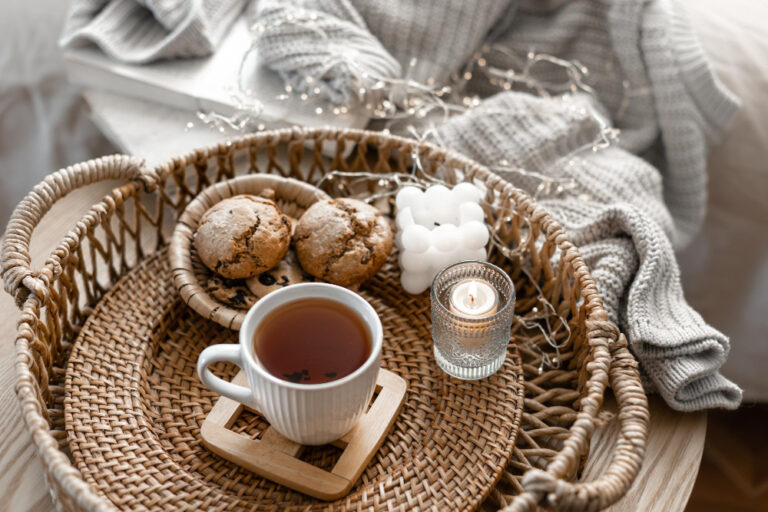 Ein Tablett mit Gebäck, einer Tasse Tee und Herzen, daneben eine Decke, wichtige Elemente von Hygge